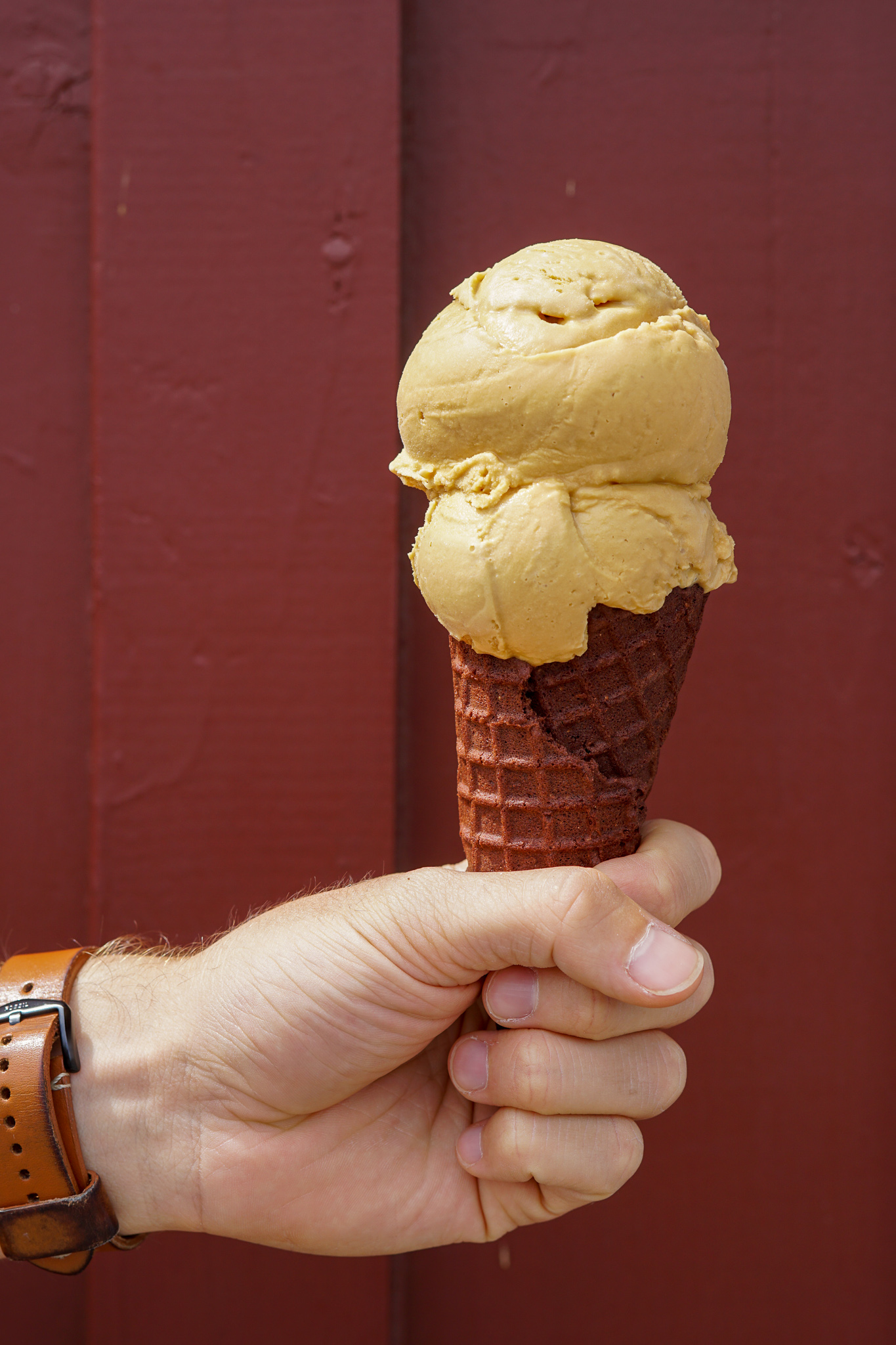 Man's hand holding a chocolate cone topped with 2 scoops of Salted Caramel ice cream