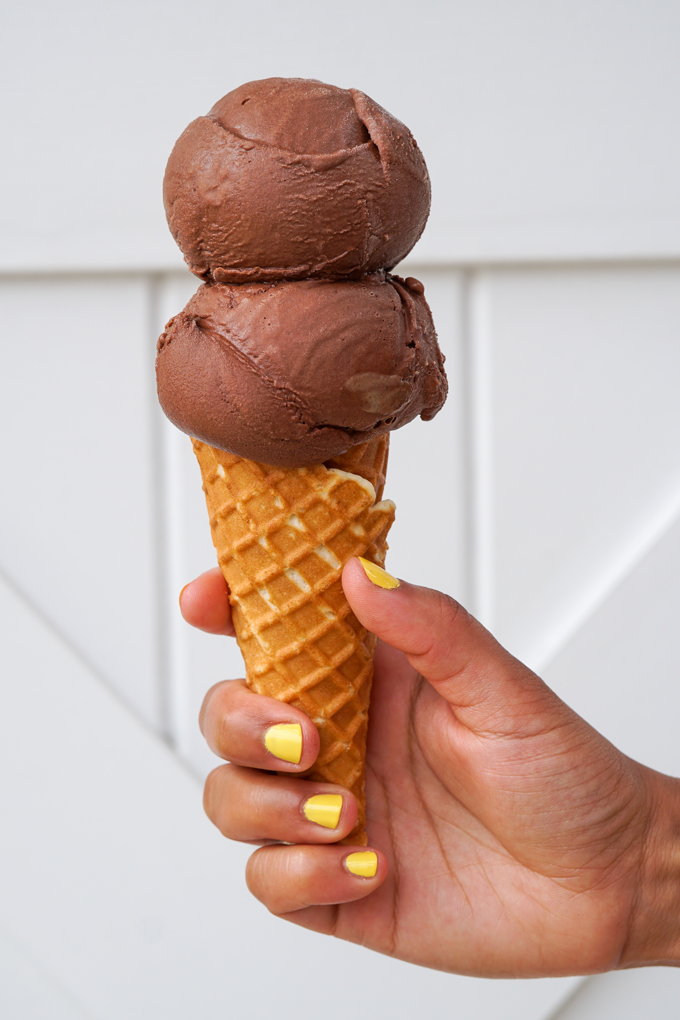 Woman's hand holding a vanilla cone topped with 2 scoops of Chocolate ice cream