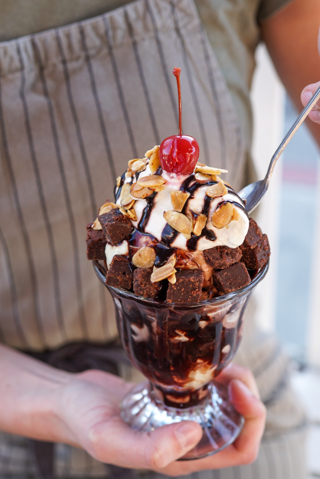 Woman's hands holding a Brownie Sundae and dipping a spoon into it