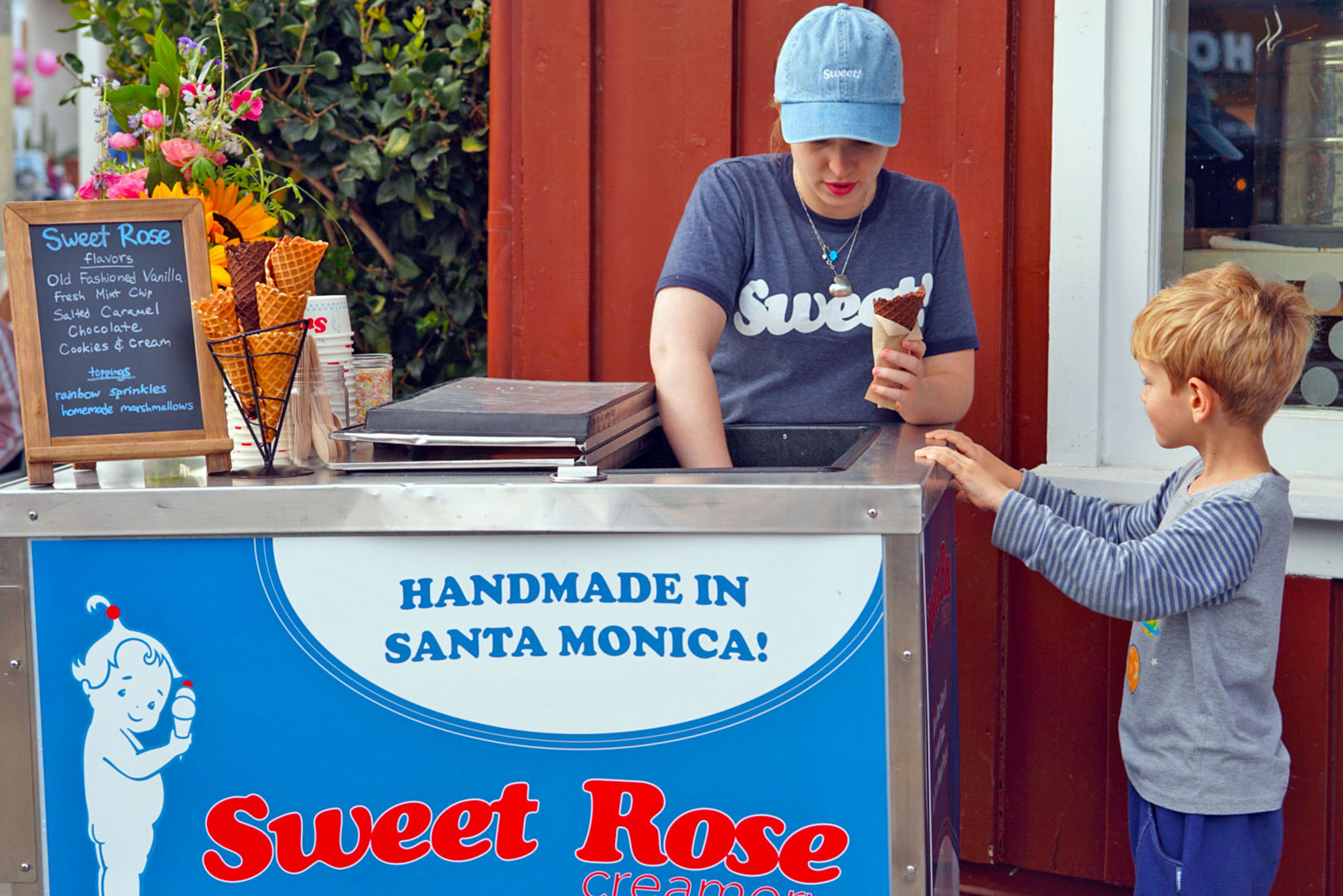 Female employee scooping ice cream from the Sweet Rose Creamery Cart with a little boy waiting at the Brentwood Country Mart