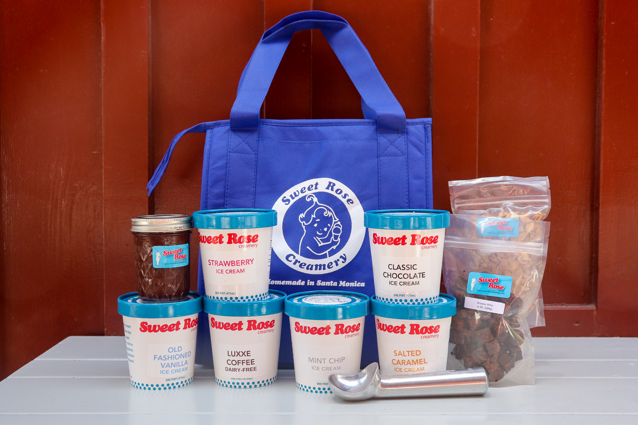 A Party Pack with a Sweet Rose Creamery cooler bag, a variety of pints, toppings, jar of hut fudge and ice cream scoop on a table