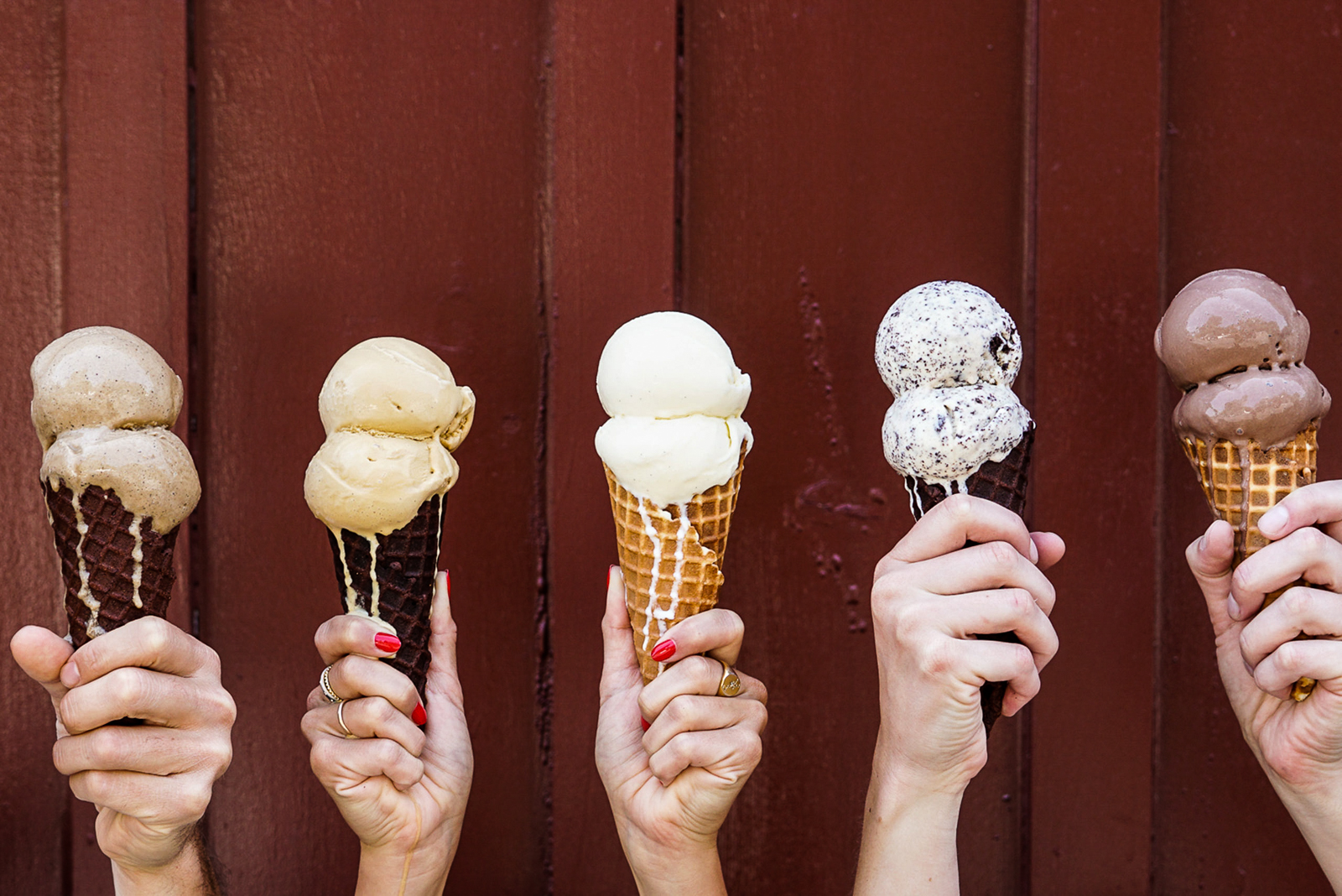 Hands holding a variety of cream cones topped with classic flavors of ice cream