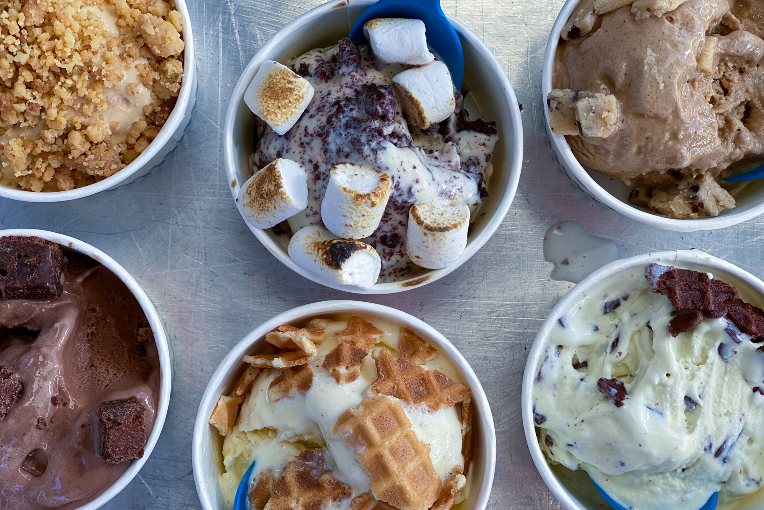 Variety-of-Classic-Flavors-&-Toppings-In-Cups Variety of classic ice cream flavors in cups topped with housemade toppings on a sheet tray
