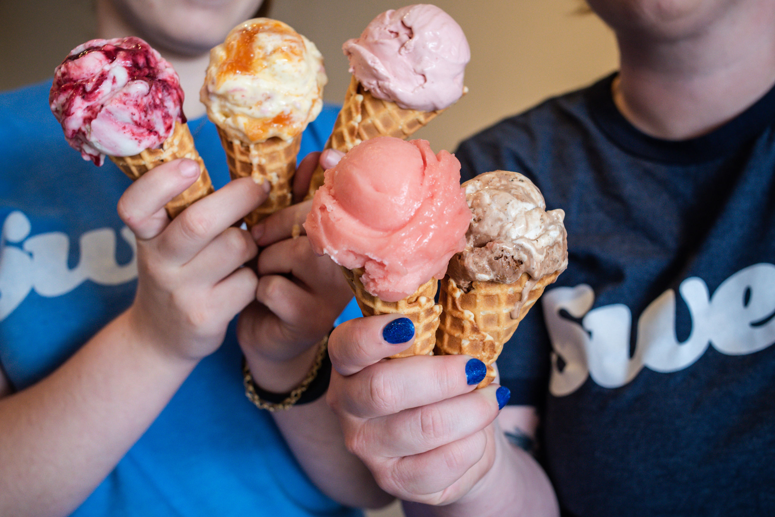 Close-up of two employees holding 6 ice cream cones filled with a variety of colorful flavors