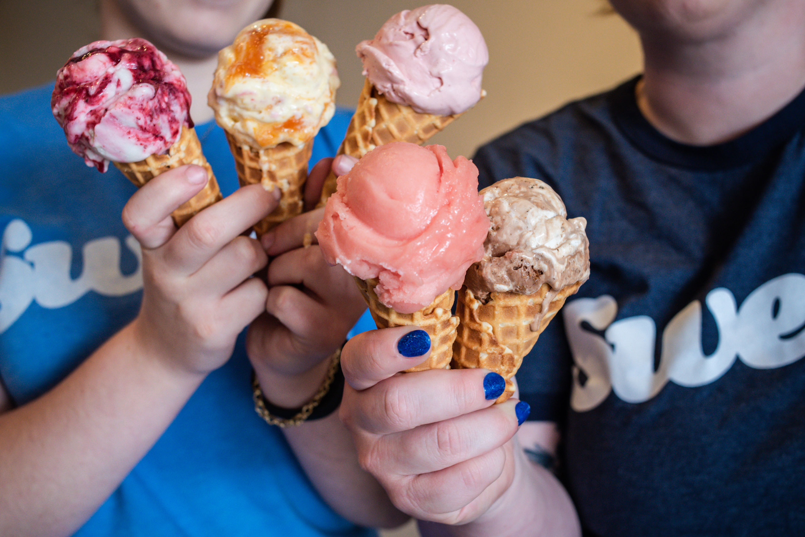 Variety-of-Summer-Flavor-Ice-Cream-Cones Close-up of two employees holding 6 ice cream cones filled with a variety of colorful flavors