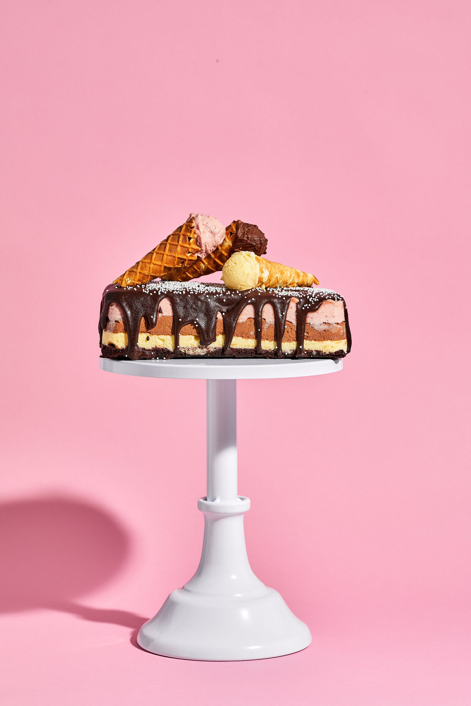 a layered cake with chocolate cake, vanilla ice cream, chocolate ice cream, strawberry ice cream and drippy hot fudge