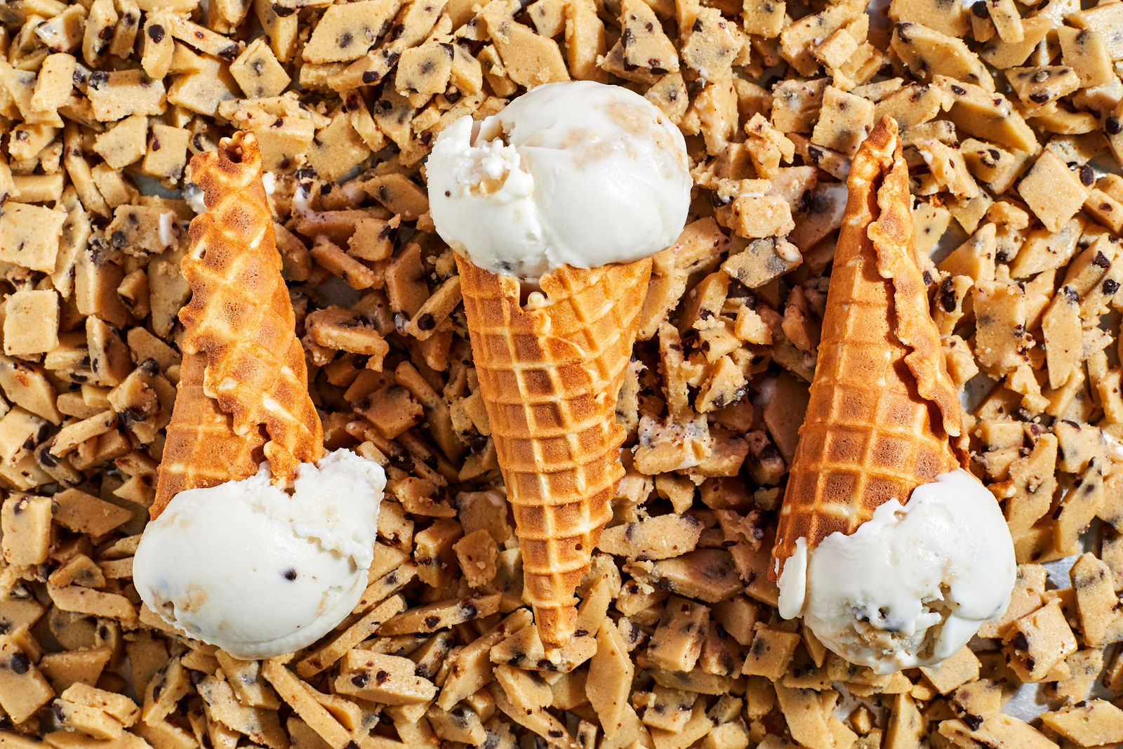 Cookie Dough Ice Cream three vanilla cones holding cookie dough ice cream, laying on a bed of cookie dough chunks