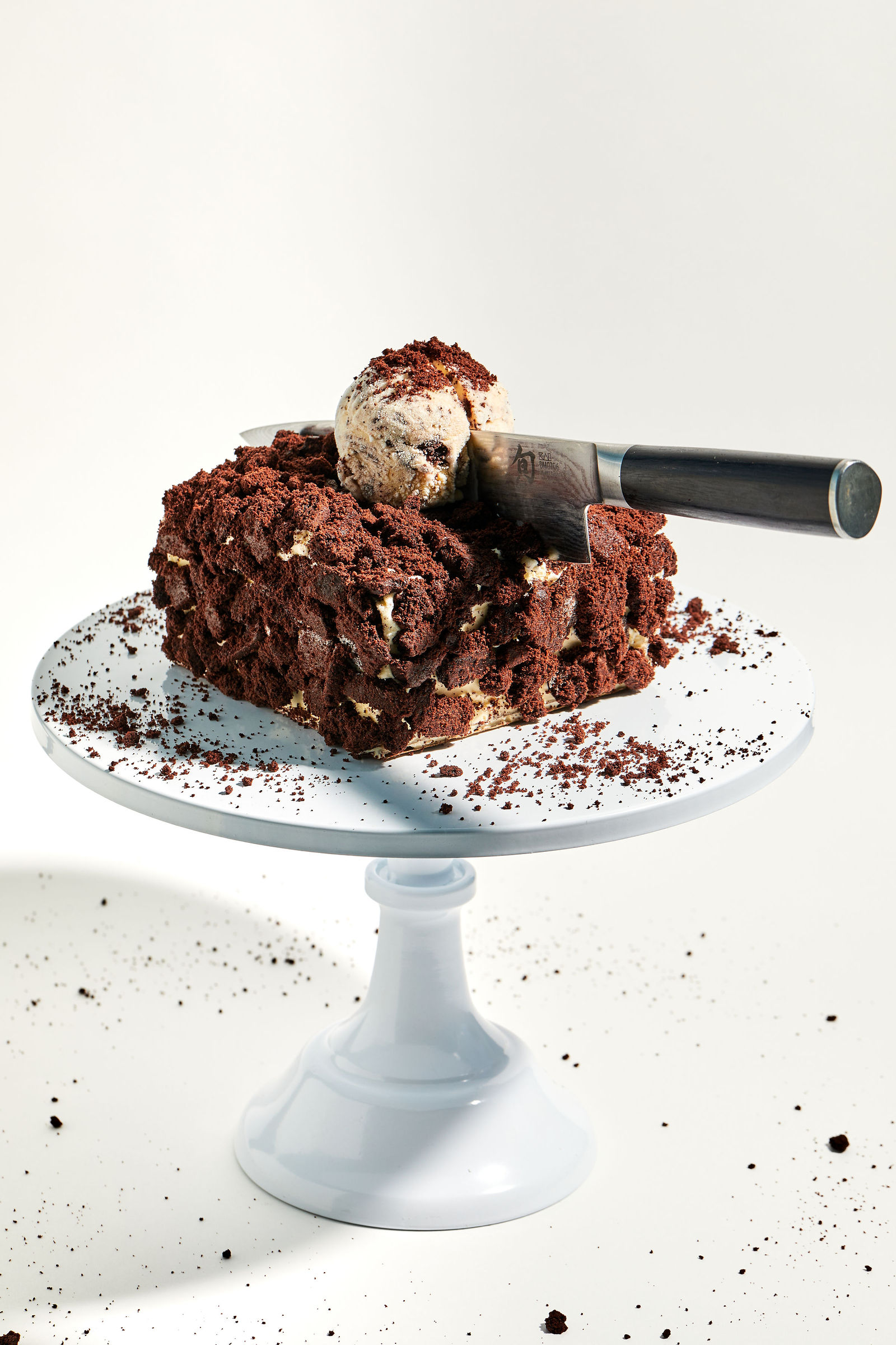 a knife slicing through a layered cake covered in chocolate cookie crumbles