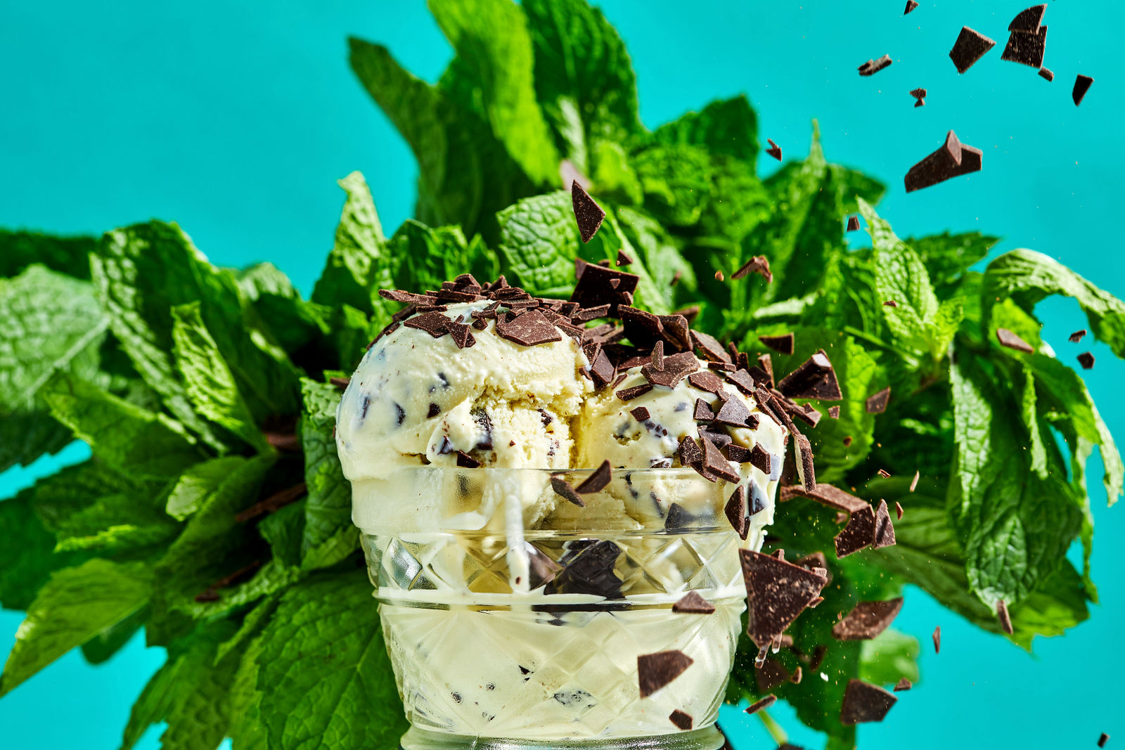 Fresh Mint Chip Ice Cream chocolate chips falling on scoops of ice cream with fresh mint leaves in the background