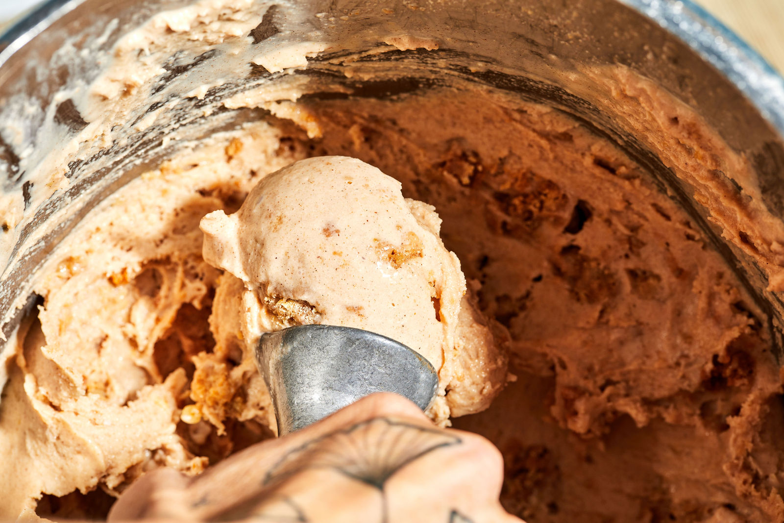 Cinnamon Oatmeal Cookie Ice Cream a hand scooping ice cream from a canister