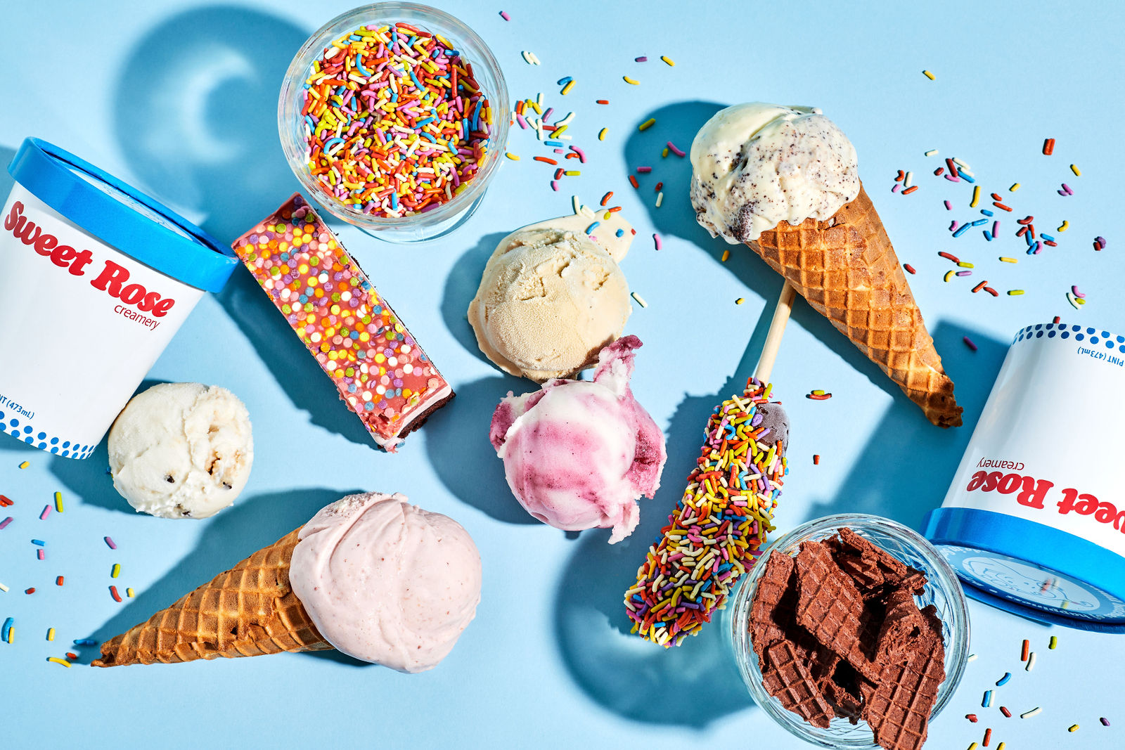 a spread of ice cream pints, cones, rainbow sprinkles and frozen novelties