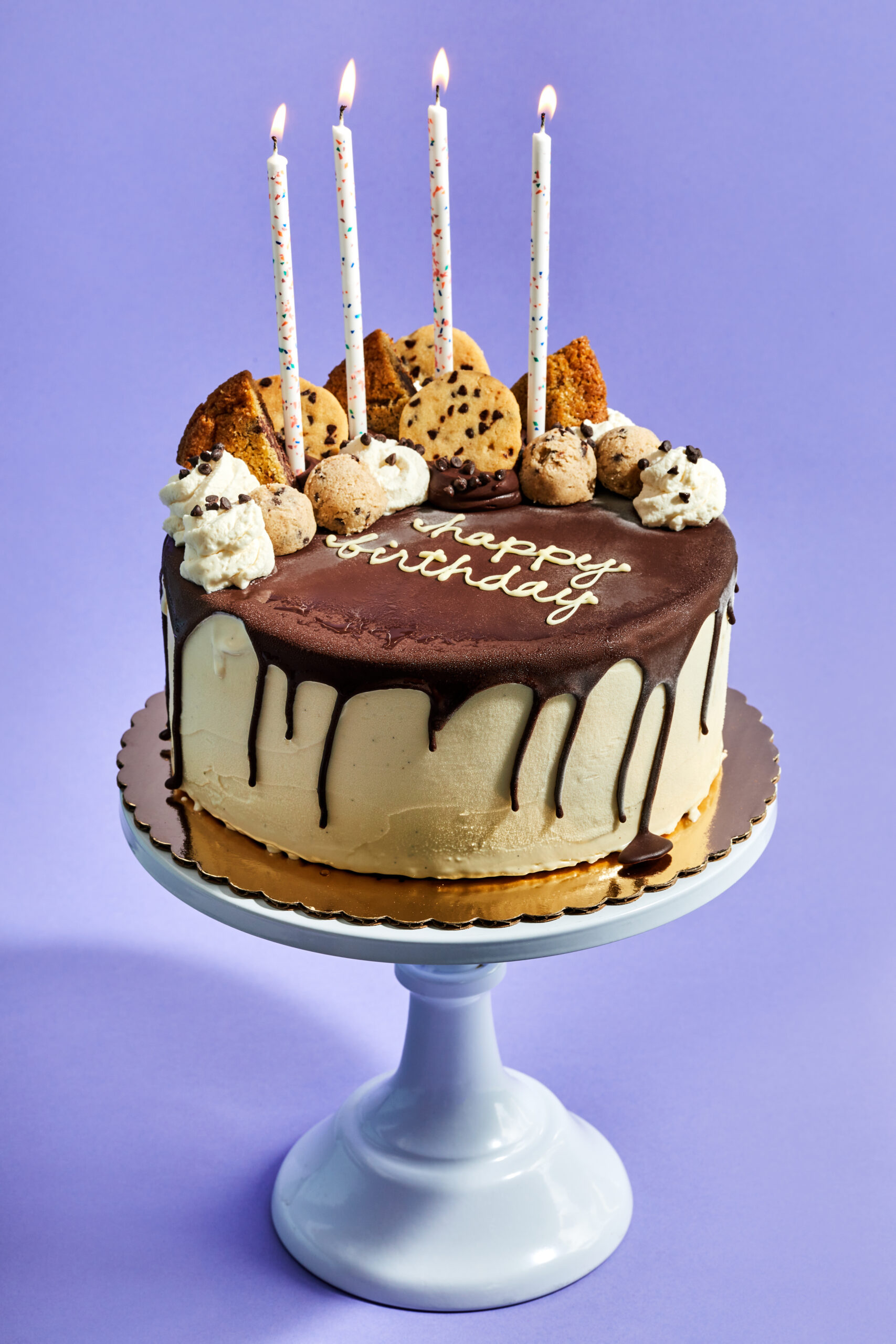 hot fudge dripping down a vanilla ice cream cake topped with Milo + Olive cookies, cookie dough balls, whipped cream and candles.