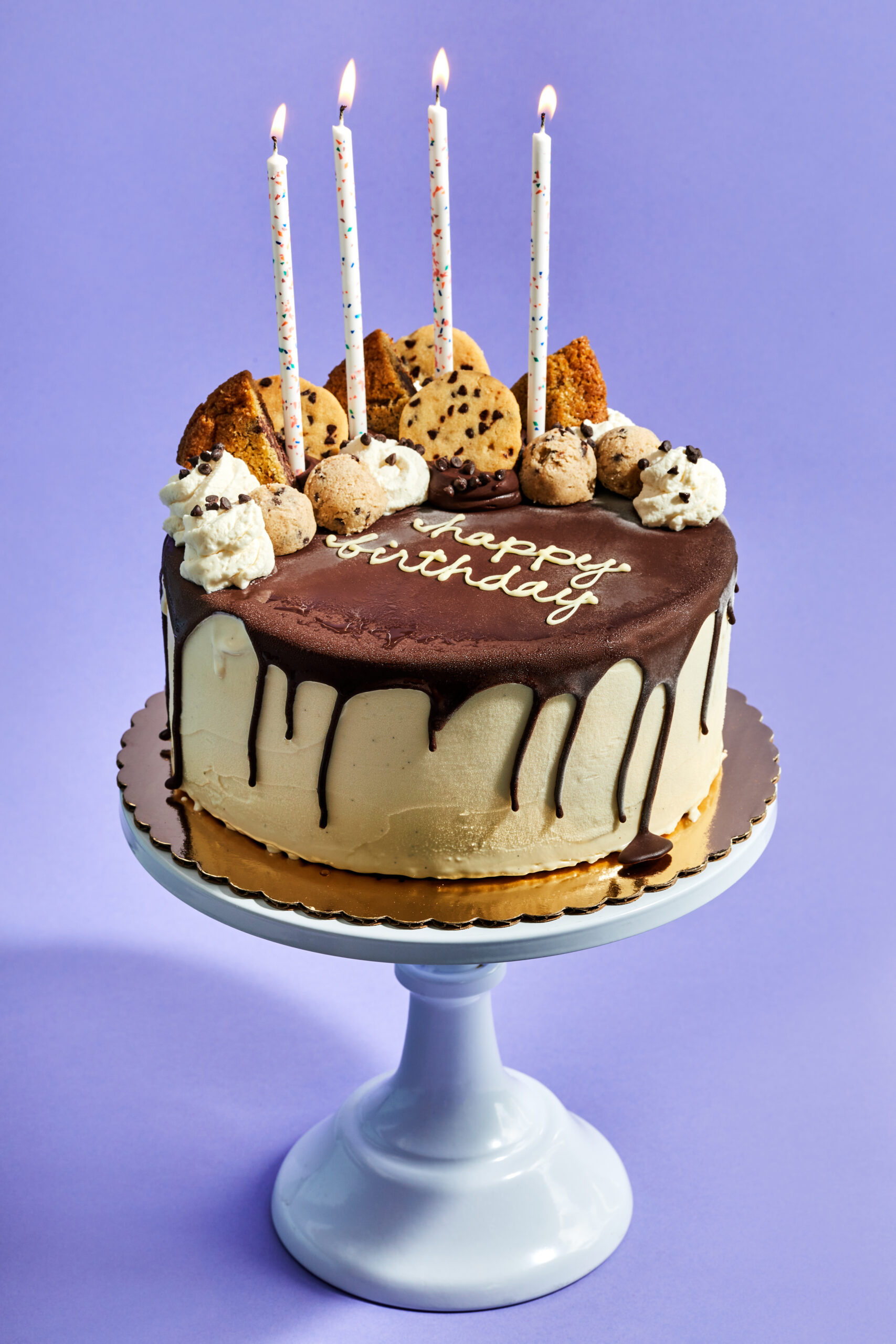 Cookie Party Cake hot fudge dripping down a vanilla ice cream cake topped with Milo + Olive cookies, cookie dough balls, whipped cream and candles.